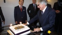 Bernie Ecclestone cutting a birthday cake with candles, surrounded by men in suits.