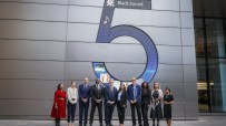 Group of diverse professionals in business attire standing in front of a UBS building with Black Sound 5 display for Black...