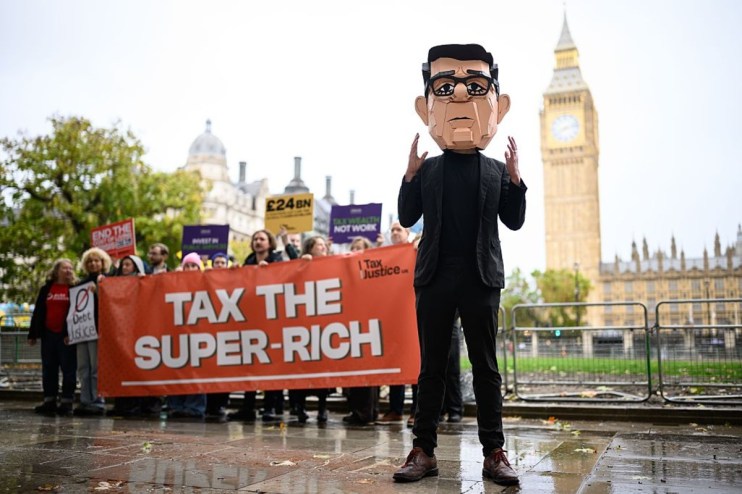 Protesters with Tax the Super-Rich banner and a Rishi Sunak caricature at a budget protest near Big Ben.