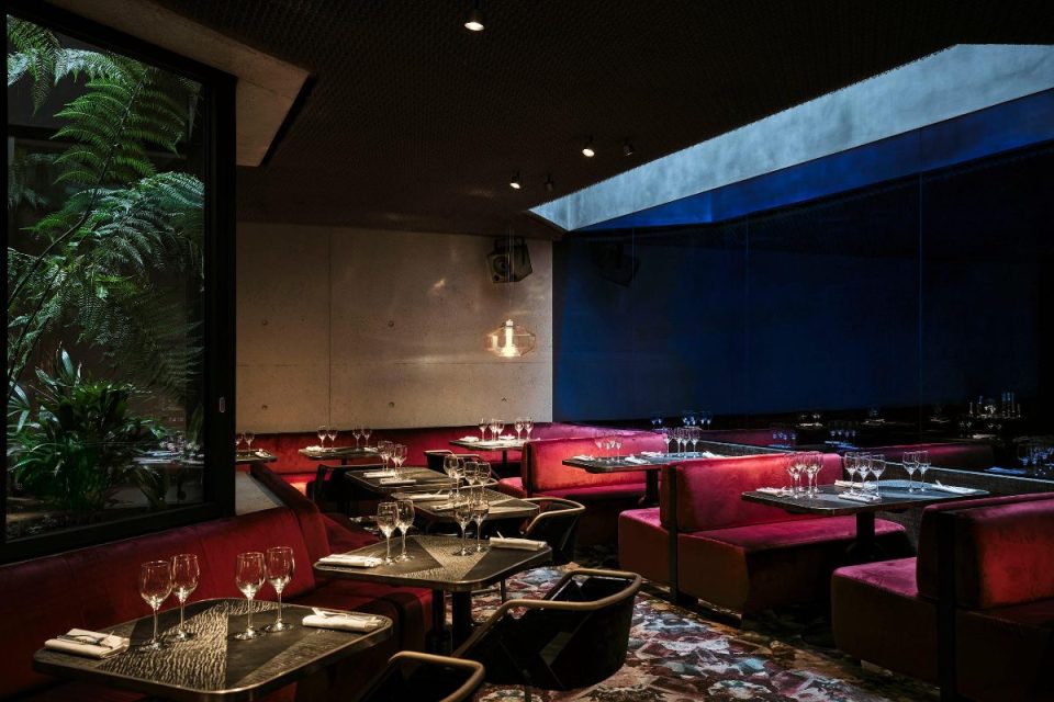 Bus Palladium restaurant interior with red velvet booths, set tables, and plants visible through a window.