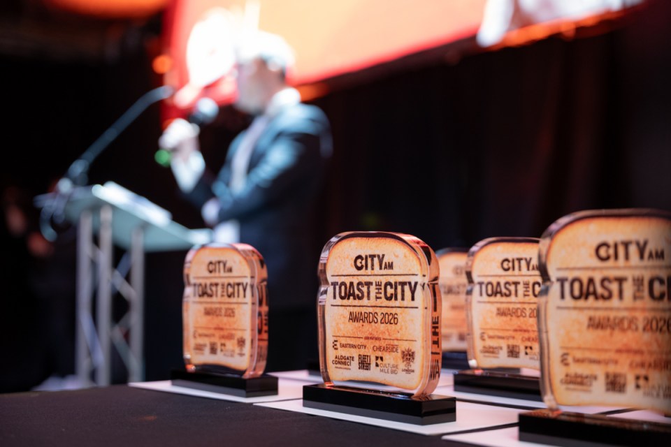 CITYAM Toast of the City Awards 2026 trophies on display with a speaker at a podium in the background.