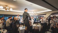 Guests and staff cheering, clapping, and singing at a lively event in a restaurant dining room.