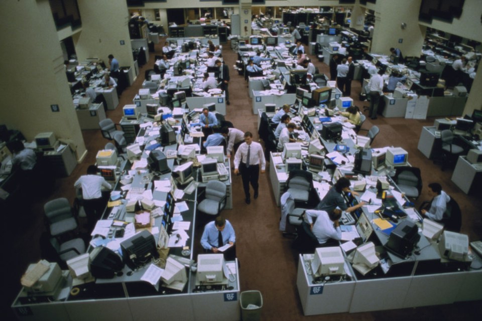Busy City of London trading floor during the Big Bang, with traders at desks surrounded by computers and papers.