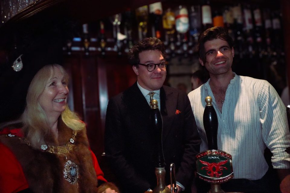 Three people, including a woman in regalia, smiling at Simpsons Tavern restaurant, Cornhill, London.