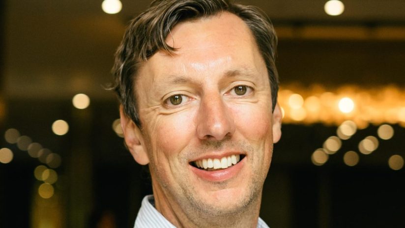 Daniel Pell smiling, a close-up headshot of a man with light brown hair and green eyes in a striped shirt