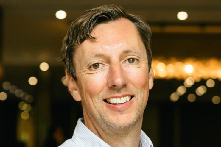 Daniel Pell smiling, a close-up headshot of a man with light brown hair and green eyes in a striped shirt