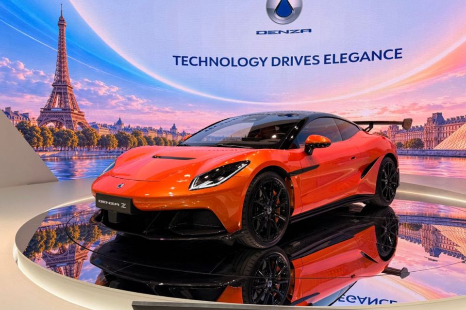 Sleek orange Denza Z 2 sports car on a reflective display stand, with a Paris cityscape backdrop and Denza branding.