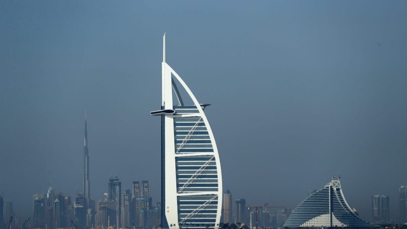 Dubai skyline with Burj Al Arab and Jumeirah Beach Hotel, Burj Khalifa in background over blue water.