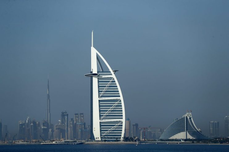 Dubai skyline with Burj Al Arab and Jumeirah Beach Hotel, Burj Khalifa in background over blue water.