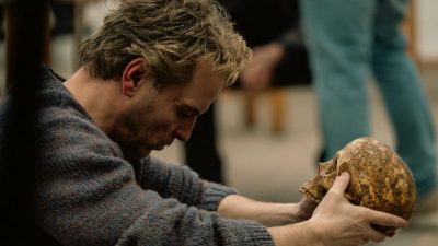 Man in a textured sweater holding a human skull, possibly Hamlet in Elsinore performance
