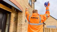 Construction worker in Bellway jacket raising hard hat in front of new brick house
