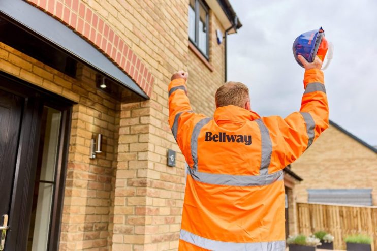 Construction worker in Bellway jacket raising hard hat in front of new brick house