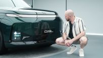 Man in striped shirt crouches next to the front of a dark green XPeng G9 electric SUV