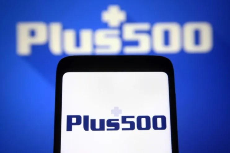 Plus500 logo on a smartphone screen, with a larger, blurred Plus500 logo in the background, against a blue backdrop