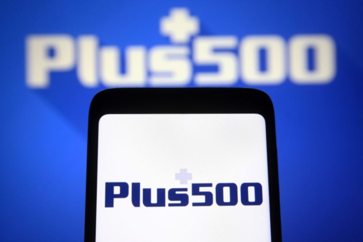 Plus500 logo displayed on a smartphone screen, with a larger, blurred Plus500 logo in the background