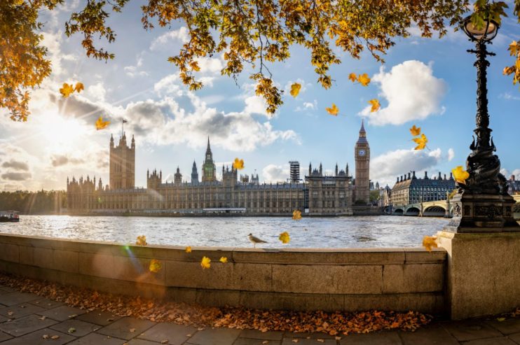 Autumn leaves falling over the River Thames with the Houses of Parliament and Big Ben in London.