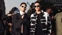 Two young men in stylish black and white streetwear, one with a floral shirt and the other in tie-dye.