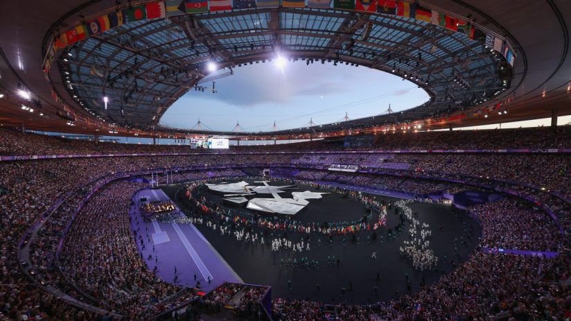 Olympic stadium interior with flags, spectators, and performers on the field during an event.