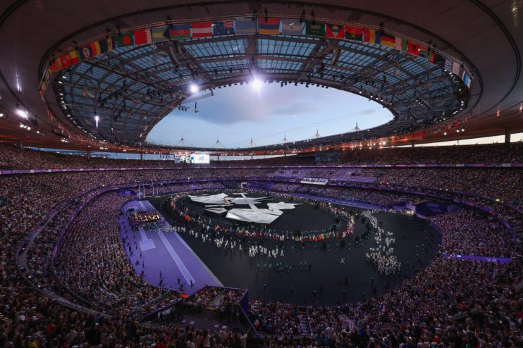 Olympic stadium interior with flags, spectators, and performers on the field during an event.