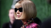 Anna Wintour in black sunglasses, blonde bob, colorful statement necklace, and a patterned top.