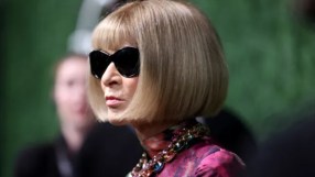 Anna Wintour in black sunglasses, blonde bob, colorful statement necklace, and a patterned top.