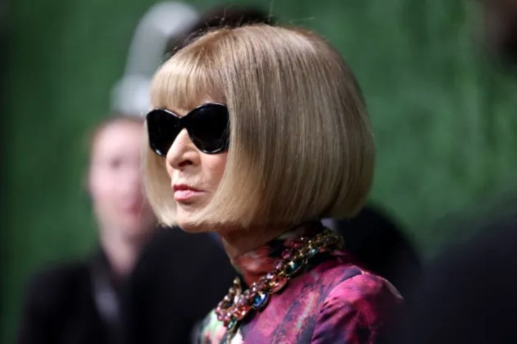 Anna Wintour in black sunglasses, blonde bob, colorful statement necklace, and a patterned top.