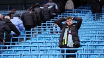 Disappointed football fan in a black puffer jacket and team scarf, hands on head, in a blue stadium crowd