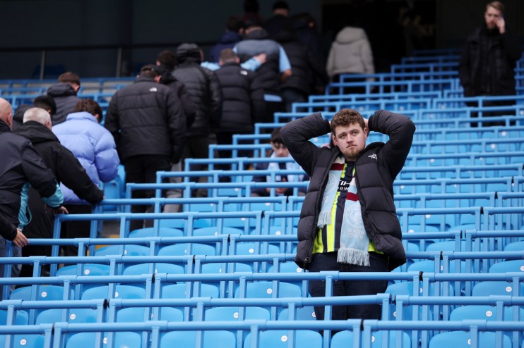 Disappointed football fan in a black puffer jacket and team scarf, hands on head, in a blue stadium crowd