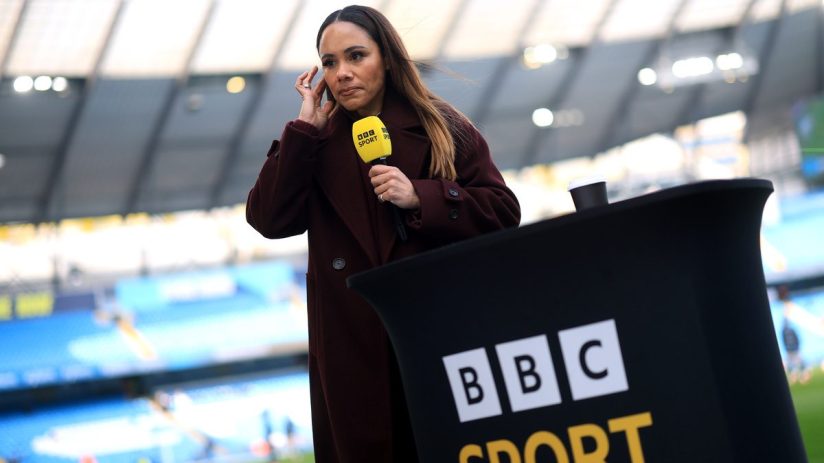 Alex Scott, former England footballer and BBC Sport pundit, reporting from a stadium pitchside with a BBC microphone.