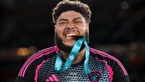 Soccer Aid player with beard bites gold medal, wearing black and pink kit, celebrating win for Unicef