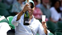 Man in sunglasses and cap spraying champagne, holding a flute at a live sport event, symbolizing high ticket prices.