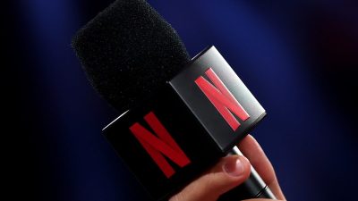 Hand holding a microphone with the Netflix logo on its cube, dark background.
