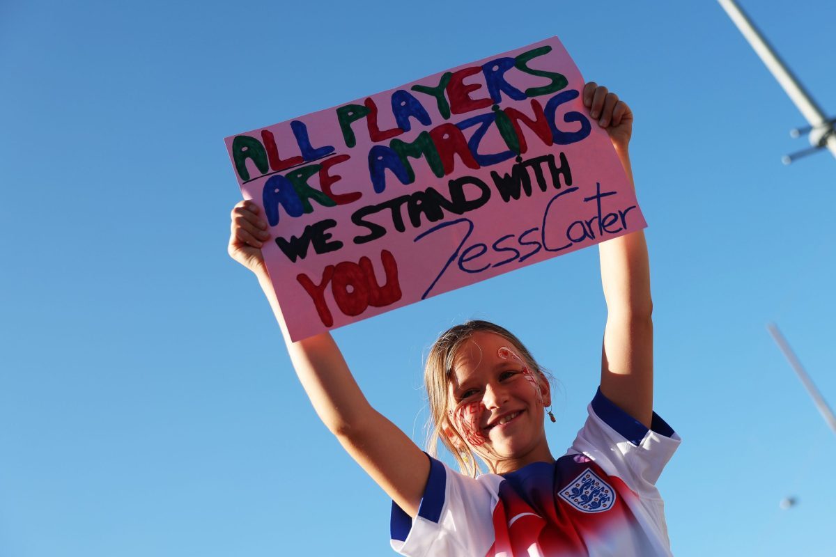 Young girl in England football shirt holds ALL PLAYERS ARE AMAZING WE STAND WITH YOU Jess Carter sign