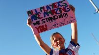 Young girl in England football shirt holds ALL PLAYERS ARE AMAZING WE STAND WITH YOU Jess Carter sign