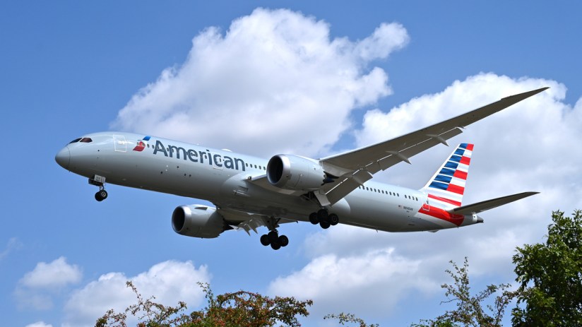 American Airlines passenger jet, a Boeing 787, in flight against a blue sky with clouds, landing gear down.
