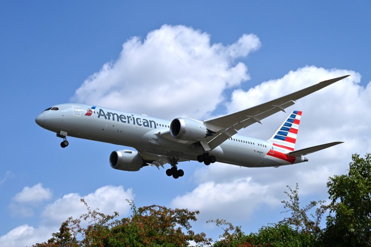 American Airlines passenger jet, a Boeing 787, in flight against a blue sky with clouds, landing gear down.