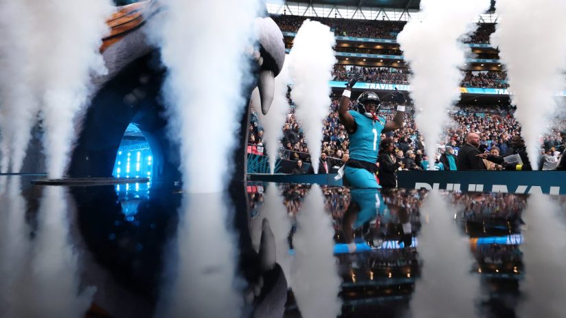 NFL player Travis Etienne Jr. of the Jacksonville Jaguars emerges from a smoky tunnel onto the field, arms raised, with fa...