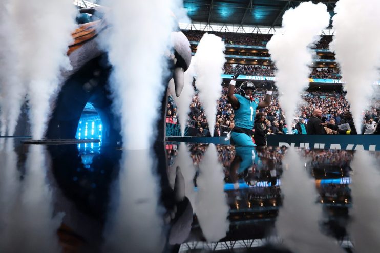 NFL player Travis Etienne Jr. of the Jacksonville Jaguars emerges from a smoky tunnel onto the field, arms raised, with fa...