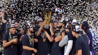 Basketball players celebrate winning the 2025 NBA Cup, holding the trophy under falling confetti.