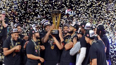 Basketball players celebrate winning the 2025 NBA Cup, holding the trophy under falling confetti.