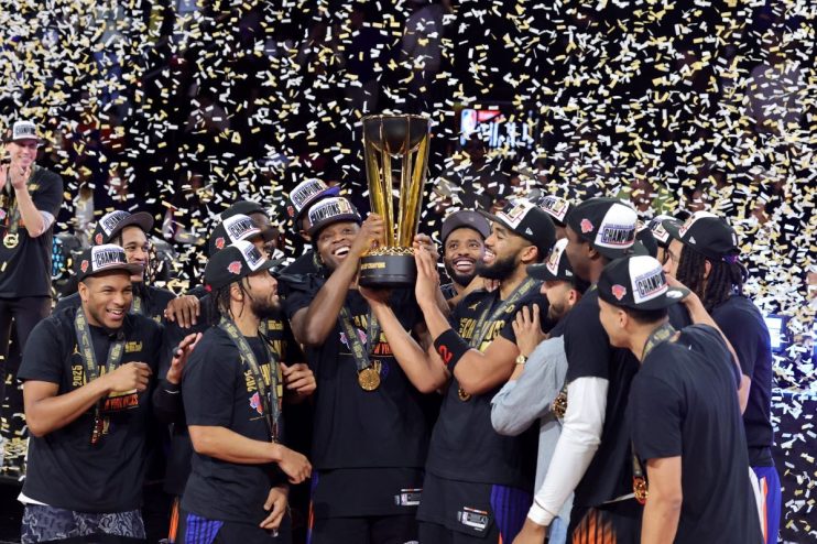 Basketball players celebrate winning the 2025 NBA Cup, holding the trophy under falling confetti.