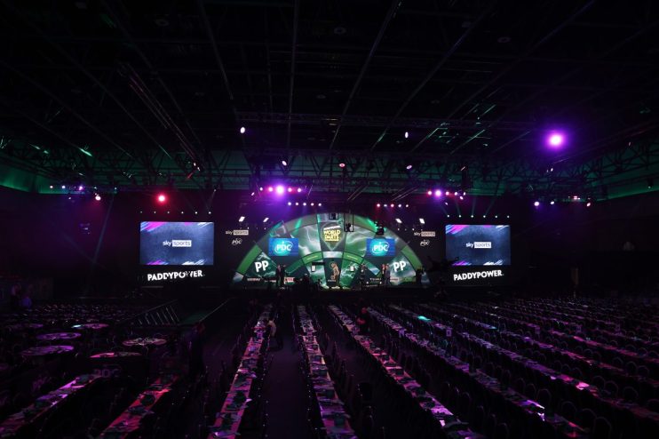Empty arena seating rows face a stage with Sky Sports and Paddy Power branding, ready for a darts event.