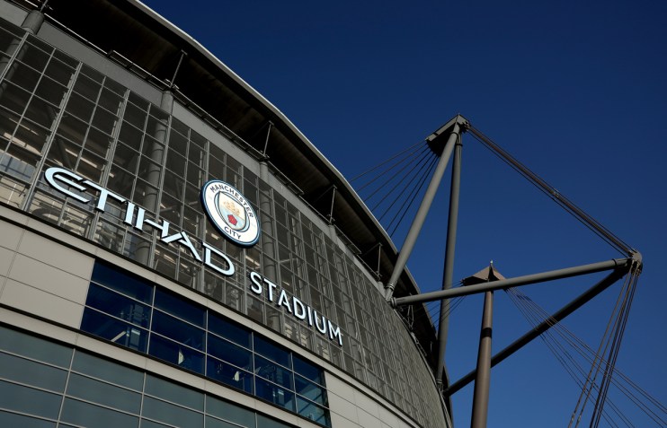 Exterior view of Etihad Stadium with Manchester City FC logo against a clear blue sky