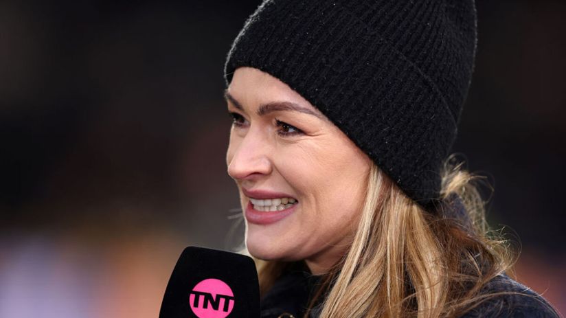 Blonde woman in a black beanie hat holding a TNT Sports microphone, smiling and looking right