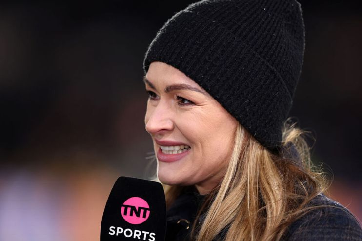 Blonde woman in a black beanie hat holding a TNT Sports microphone, smiling and looking right