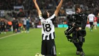 Newcastle United player Osula celebrating a goal on the pitch with arms raised, a cameraman nearby.