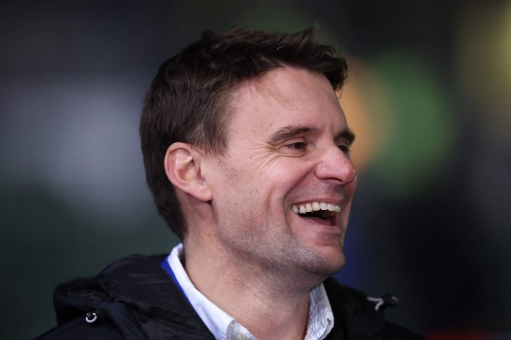 Close-up of a man laughing, looking right, with a dark jacket and white collared shirt