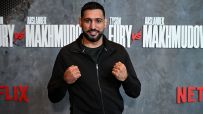 Amir Khan, former boxing champion, clenches fists in front of a Fury vs Makhmudov promotional backdrop