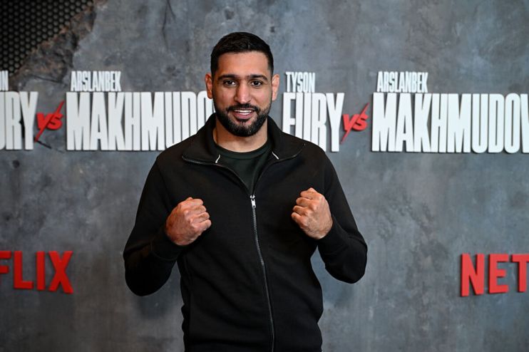 Amir Khan, former boxing champion, clenches fists in front of a Fury vs Makhmudov promotional backdrop