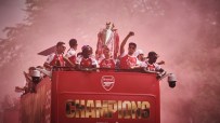 Arsenal team on a red double-decker bus parade, celebrating with the Premier League trophy amidst red smoke.